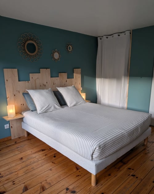 Chambre moderne au Mas des Landes avec murs bleu-vert, tête de lit style château en bois, literie rayée et vue sur le jardin