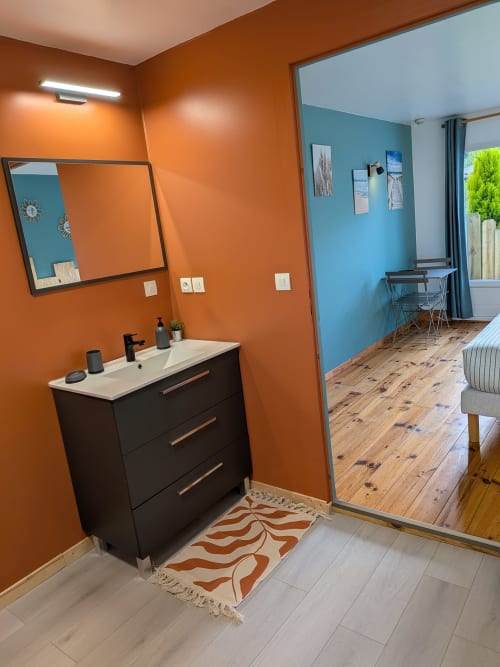Salle de bain moderne aux murs orangés, vasque noire et miroir dans la chambre Baïne du mas des Landes