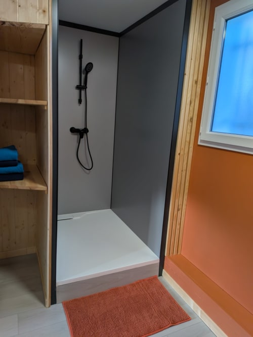 Douche moderne aux murs gris, robinetterie noire et base blanche dans la Chambre Baïne au Mas des Landes
