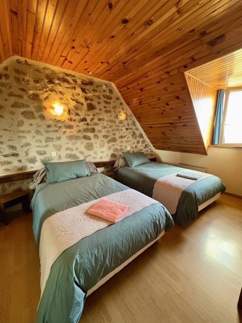 Zweibettzimmer im Lo Soulenquo B&B in Golinhac mit Steinwänden, Holzdecke und Bergblick
