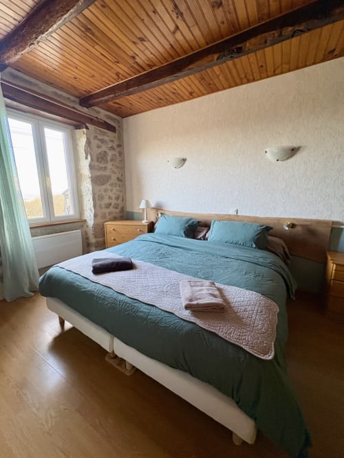 Chambre rustique aux poutres apparentes, lit queen-size avec parure turquoise, murs en pierre et vue sur les montagnes à Lo Soulenquo B&B