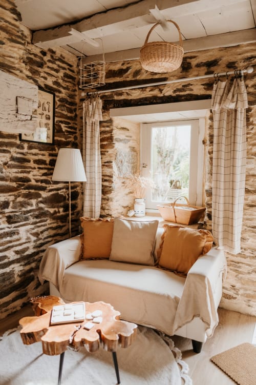 Intérieur cosy du gîte en pierre aux Granges De Pil Bara avec canapé crème, poutres bois et décoration rustique à Langoat