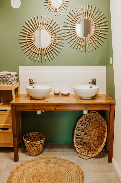 Salle de bains chaleureuse avec doubles vasques, meuble en bois, murs verts et miroirs tressés décorés aux Granges De