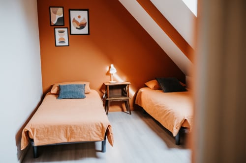 Chambre lumineuse aux Granges De Pil Bara avec deux lits, murs orangés, puits de lumière et décoration moderne à Langoat, France.