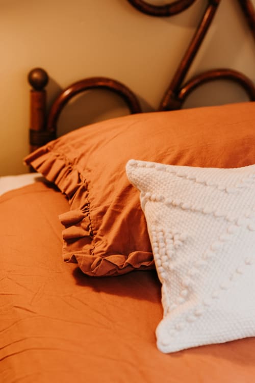 Lit douillet avec une couette à volants orangés et un oreiller matelassé blanc à La grange Romarin, Les Granges De Pil Bara