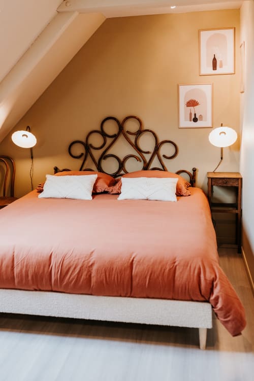 Chambre douillette aux Granges de Pil Bara à Langoat avec literie corail, tête de lit décorée, oreillers blancs et nuances ocre chaud