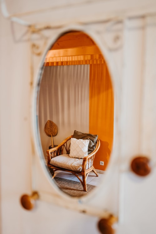 Fauteuil en bois avec coussins reflété dans un miroir ovale au gîte Les Granges De Pil Bara, Langoat