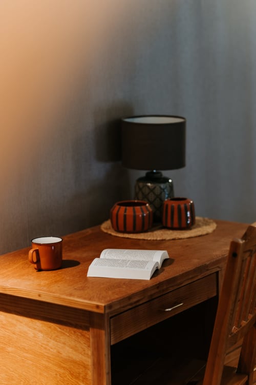 Bureau en bois avec un livre ouvert, une tasse orange et une lampe noire au gîte Les Granges De Pil Bara