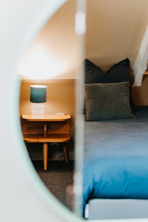 Alcôve de chambre moderne au gîte Les Granges De Pil Bara à Langoat, avec table de nuit en bois, lampe turquoise et oreillers