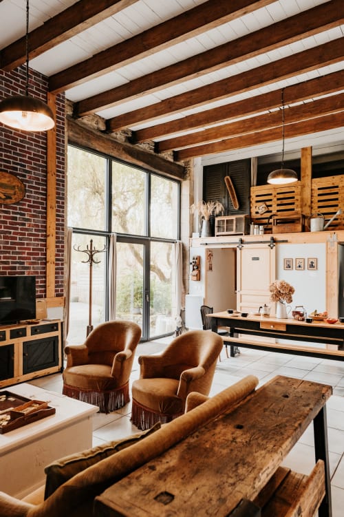 Intérieur rustique moderne avec poutres apparentes, fauteuils cognac, cuisine et grandes fenêtres aux Granges de Pil