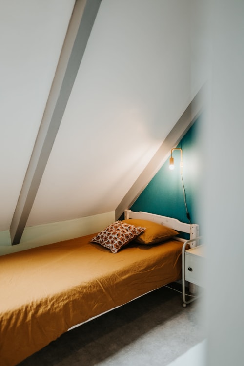 Chambre cosy sous les toits aux Granges de Pil Bara à Langoat, France avec literie moutarde et mur d'accent bleu canard