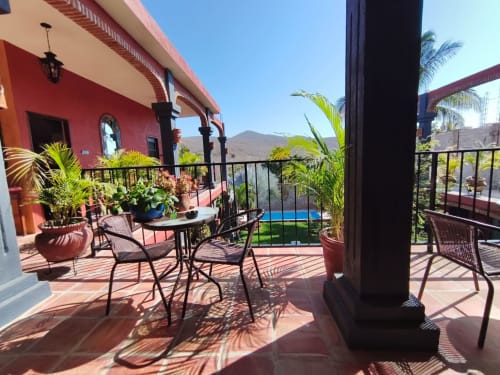 Zona de terraza de Casa Punta Perula con arquitectura colonial roja, plantas de palma, vistas de montañas y piscina en Jalisco, México