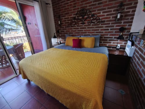 Dormitorio luminoso en Casa Punta Perula con ropa de cama amarilla, pared de ladrillo visto y balcón con vista al océano en Punta Perula, México