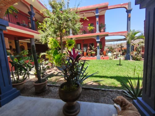 Patio de Casa Punta Perula con arquitectura colonial roja, plantas exuberantes y césped verde en Jalisco, México