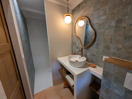 Modern bathroom at Domaine de Pelican with white vessel sink, wooden-framed mirror, pendant lights, and gray tile walls