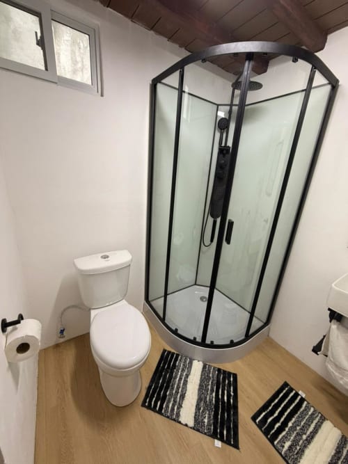 Modern bathroom at Chalets Vistas del Poas with white toilet, corner shower enclosure, wood flooring, and striped bath mats