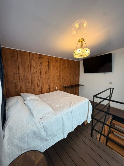 Modern bedroom at Chalets Vistas del Poas with queen bed, wooden headboard, flat-screen TV, and dark wood flooring in