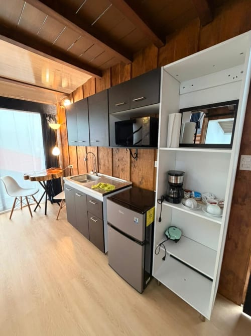 Modern kitchenette at Chalets Vistas del Poas with stainless steel appliances, white shelving, and wooden accents overlooking