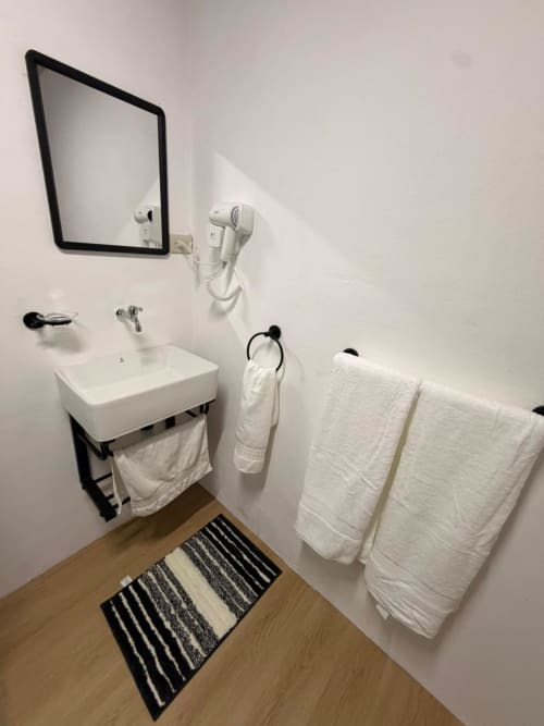 Modern bathroom at Chalets Vistas del Poas with white sink, mirror, towel racks, and striped mat on wooden floor