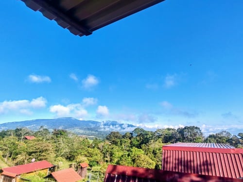 Mountain view from Chalets Vistas del Poas balcony overlooking lush Costa Rican landscape and red-roofed buildings