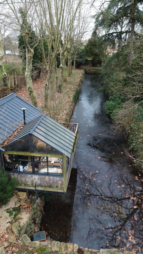 Cabine en verre moderne au Domaine ForRest à Lay, France, dominant un ruisseau paisible entouré d'arbres nus et de forêts