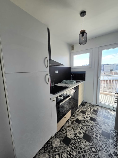 Cuisine contemporaine de l'appartement Le Sympa au NN Patrimoine, Douvaine, avec plan de travail noir, armoires blanches et sol à motifs