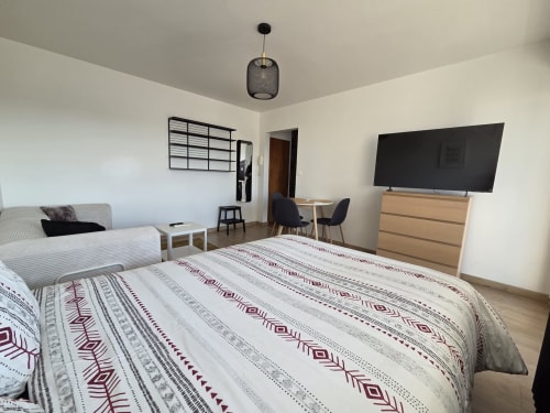 Chambre moderne NN Patrimoine à Douvanie avec lit double, TV, canapé, linge géométrique et équipements appartement