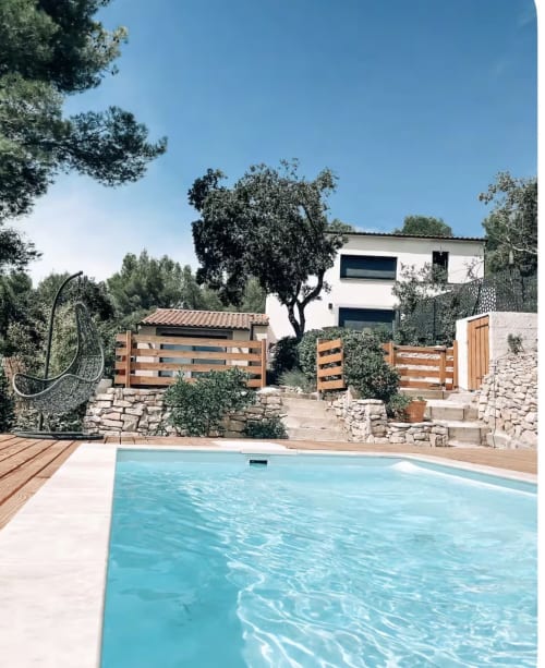 Moderne Villa mit türkisblauem Swimmingpool, Holzterrasse, Natursteinmauern und üppigem Mittelmeergartenambiente bei La Conciergerie De