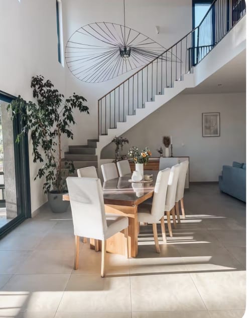 Modernes Esszimmer der Villa La Conciergerie mit Holztisch, cremefarbenen Stühlen, geometrischer Pendelleuchte und Treppe