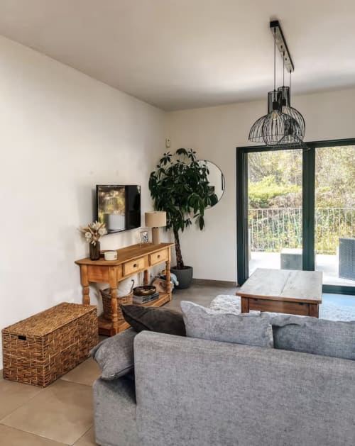Helles modernes Wohnzimmer mit grauem Sofa, Holzkonsole, Topfpflanze und schwarzer Pendelleuchte mit Blick auf den Poolbereich