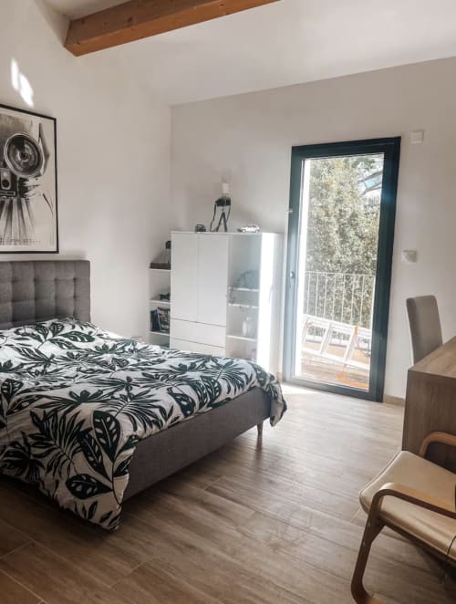 Modernes Schlafzimmer in der Villa La Conciergerie De Franck mit gemusterter Bettwäsche, weißem Stauraum und Terrassenzugang mit Poolblick