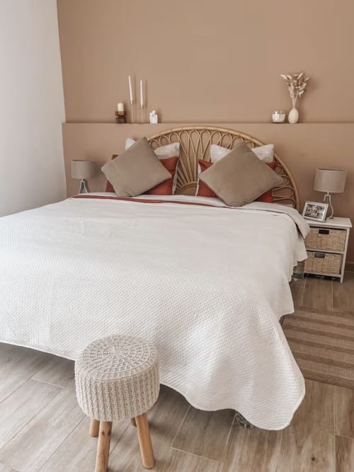 Elegantes Schlafzimmer in der Villa La Conciergerie De Franck mit Flechtbett, neutralen Tönen, weißer Steppbettwäsche und Beistelltisch