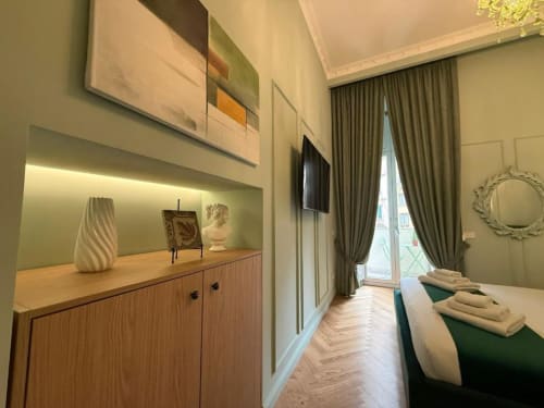 Modern hotel room at Residenza Seconnino Naples with city view balcony, green accent wall, wooden cabinet, and flat-screen TV