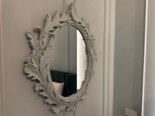 Ornate white oval mirror with baroque frame on beige wall at Residenza Seconnino hotel in Naples