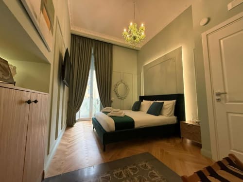 Elegant double bedroom at Residenza Seconnino Naples with green walls, black bed, chandelier, and balcony city view