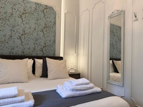 Elegante camera matrimoniale alla Residenza Seconnino a Napoli con carta da parati floreale, specchio e asciugamani freschi sul letto