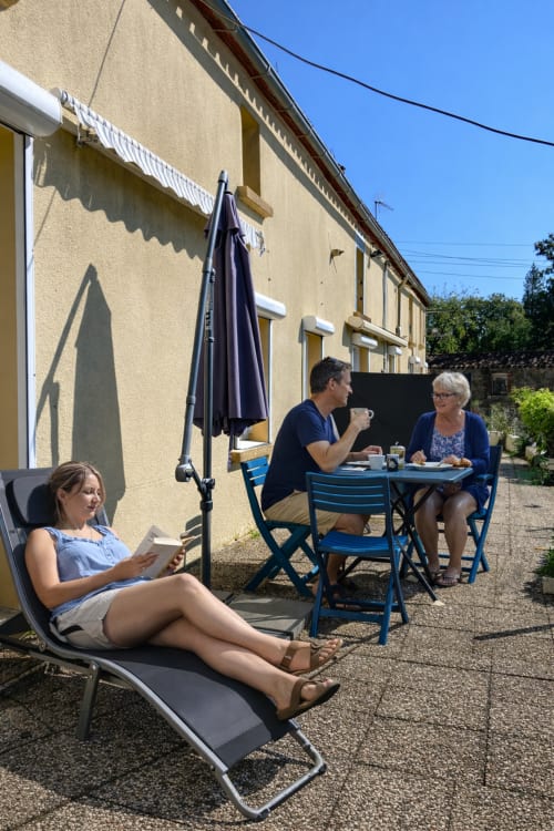 Des clients se détendent sur la terrasse ensoleillée du Gîte Le Petit Moulin à Pouzauges, profitant de l'espace extérieur et de la restauration