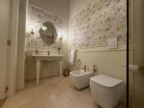 Bagno elegante della Residenza Seconnino a Napoli con carta da parati floreale, lavabo su piedistallo, bidet, wc e specchio rotondo