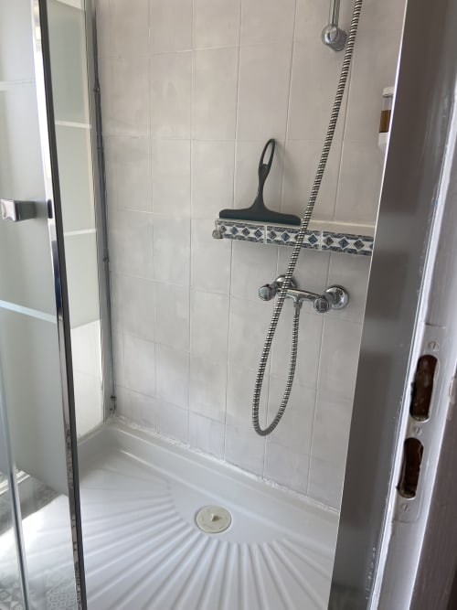 Salle de douche moderne avec carrelage blanc, frise décorative, pommeau de douche pluie et raclette à la maison d'hôtes Le Petit Moulin