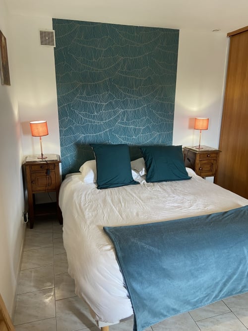 Chambre cosy du gîte Le Petit Moulin à Pouzauges avec tête de lit motifs bleu-vert, literie blanche et éclairage chaleureux