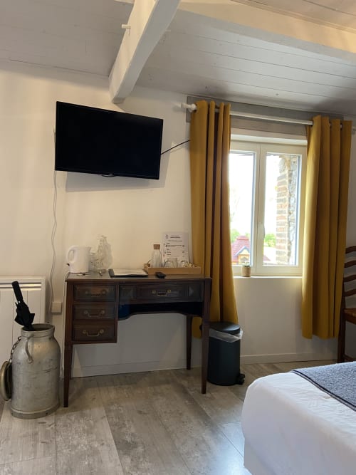 Chambre moderne au Petit Moulin à Pouzauges avec bureau, télévision, rideaux jaunes, poutres en bois et lit