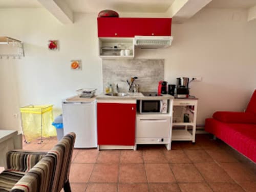 Cuisine studio et espace de vie avec rangements rouge et blanc, micro-ondes et canapé au Gîte du Mercadal à Verniolle