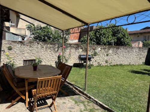 Terrasse ombragée du gîte avec table et chaises en bois, murs en pierre et pelouse verdoyante aux Pujols en Ariège.