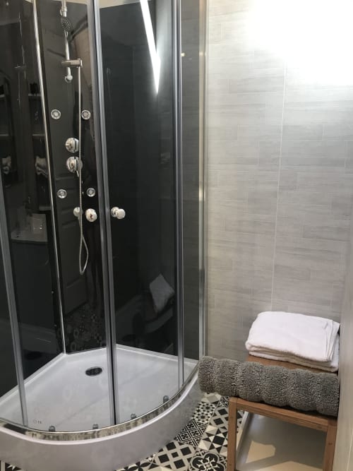Salle de douche moderne aux carrelages noir et gris, serviettes blanches sur banc en bois à la maison d'hôtes Le Petit Moulin
