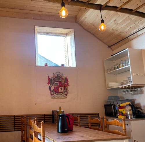 Salle à manger rustique avec poutres en bois, blason héraldique et luminaires suspendus au Petit Moulin, Pouzauges