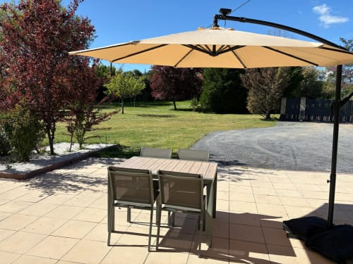 Coin détente ombragé au Jardin d'Elusa avec parasol, table et chaises vue sur les jardins
