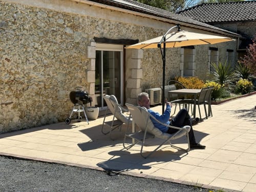 Hôte se relaxant sur la terrasse du Jardin d'Elusa, Eauze (France), architecture en pierre et parasol