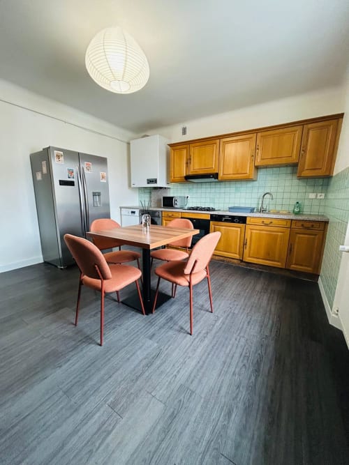 Cuisine et salle à manger modernes de l'appartement à Gérardmer avec armoires en bois, appareils en acier inoxydable et chaises corail