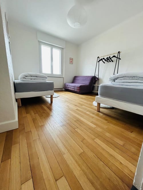 Chambre lumineuse à Gérardmer avec deux lits, canapé violet, parquet, et vue sur le lac