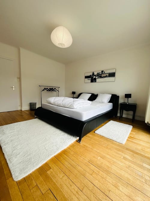 Chambre moderne avec lit noir, linge blanc, parquet et tapis blanc à La Conciergerie des Lacs